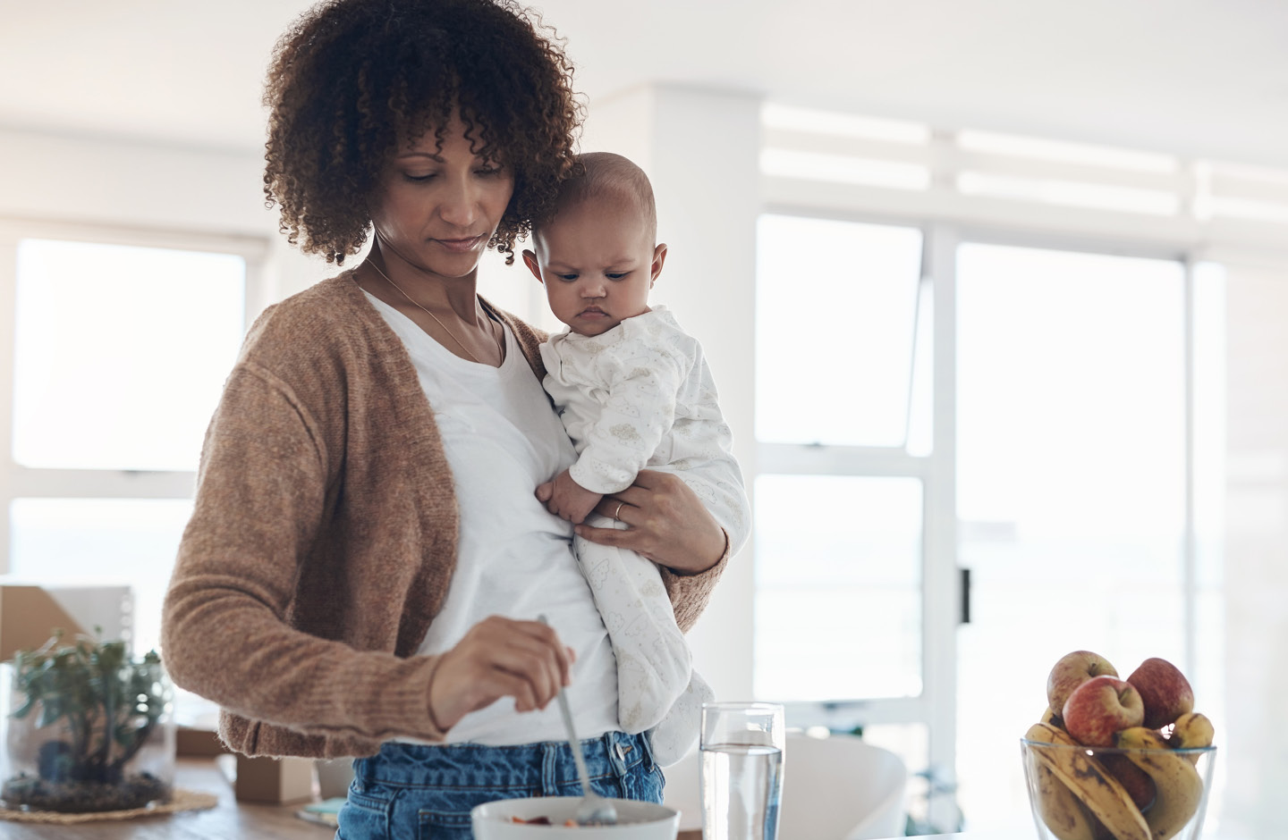 Mutter mit Baby auf dem Arm bereitet Müsli zu