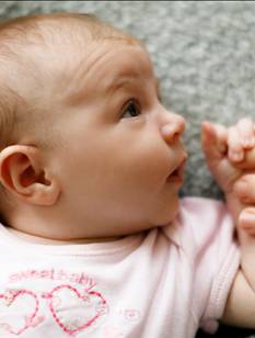 Baby auf Wolldecke schaut zur Mutter und greift ihren Zeigefinger