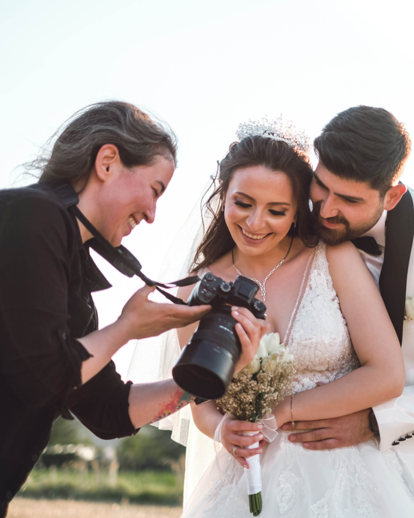 Hochzeitspaar und Fotografin gucken sich die Bilder auf der Kamera an.