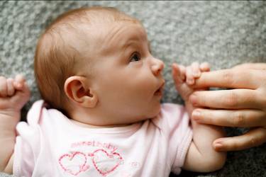 Baby auf Wolldecke schaut zur Mutter und greift ihren Zeigefinger