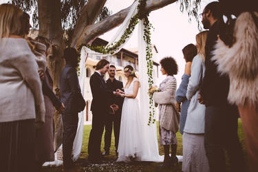 Young couple getting married with bride giving groom wedding ring at ceremony with multi-ethnic friends
