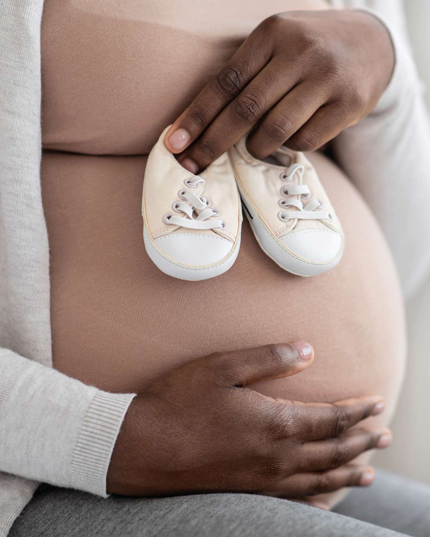 3. Trimester: Mama hält Babyschuhe vor Babybauch.