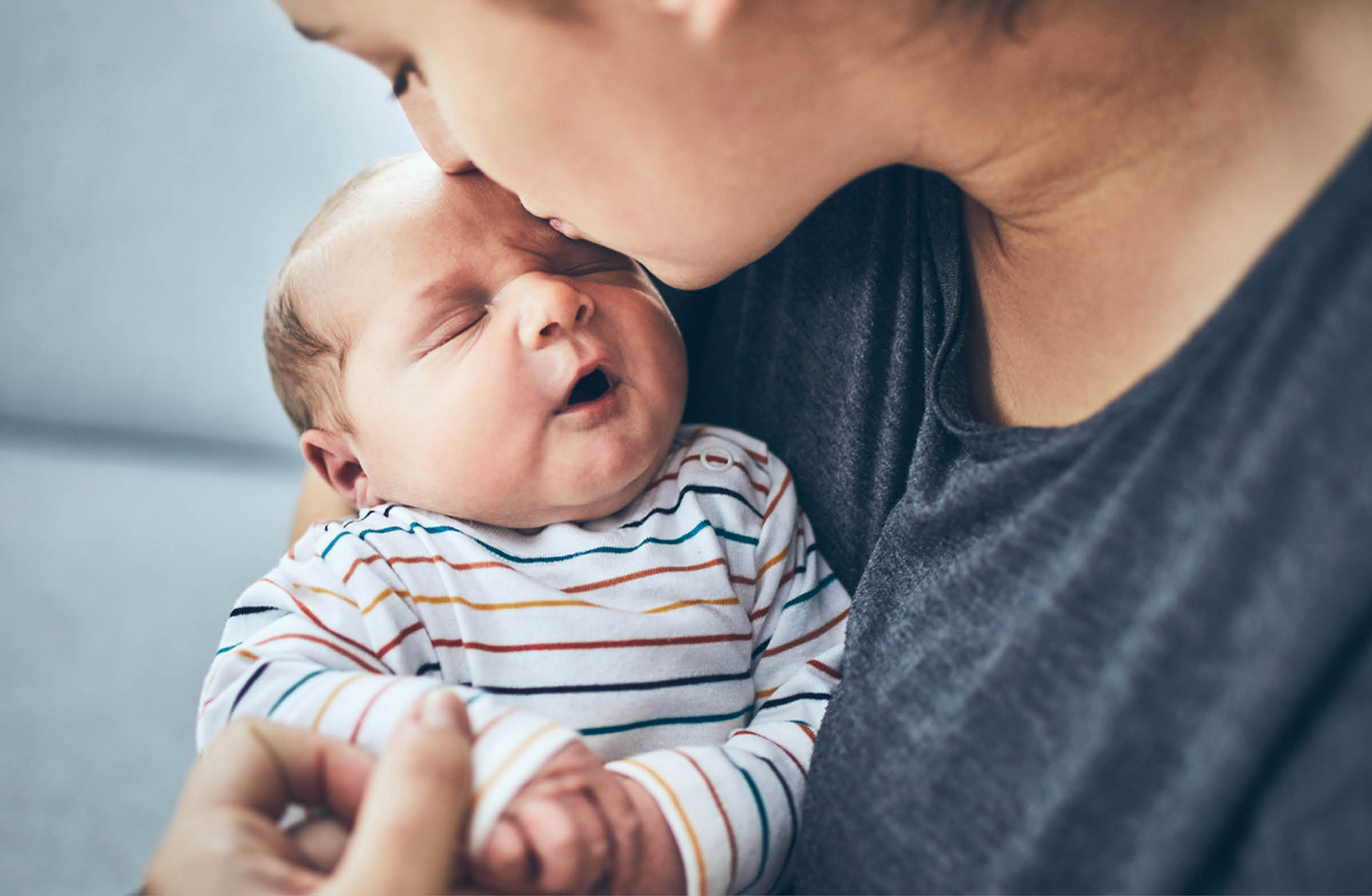 Neugeborenes schläft auf dem Arm der Mutter. Die Mutter küsst ihr Baby auf die Stirn.