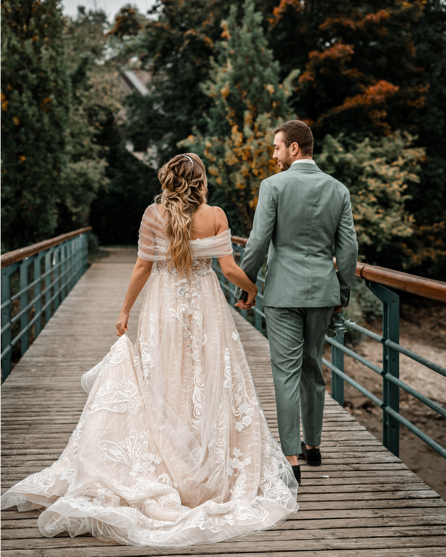 Hochzeitspaar geht Hand in Hand über eine Holzbrücke