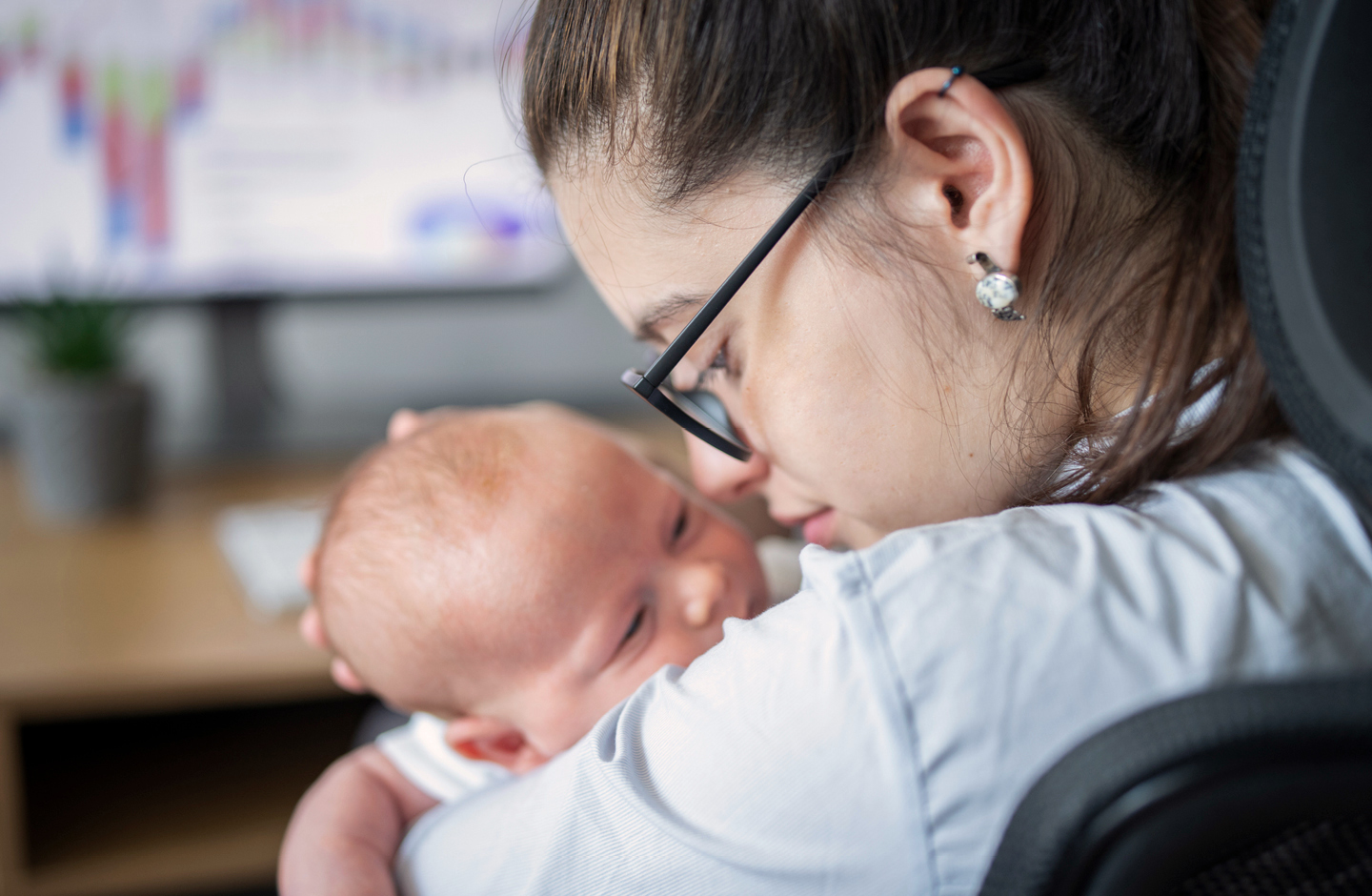 Mutter mit Baby auf dem Arm am Laptop im Homeoffice