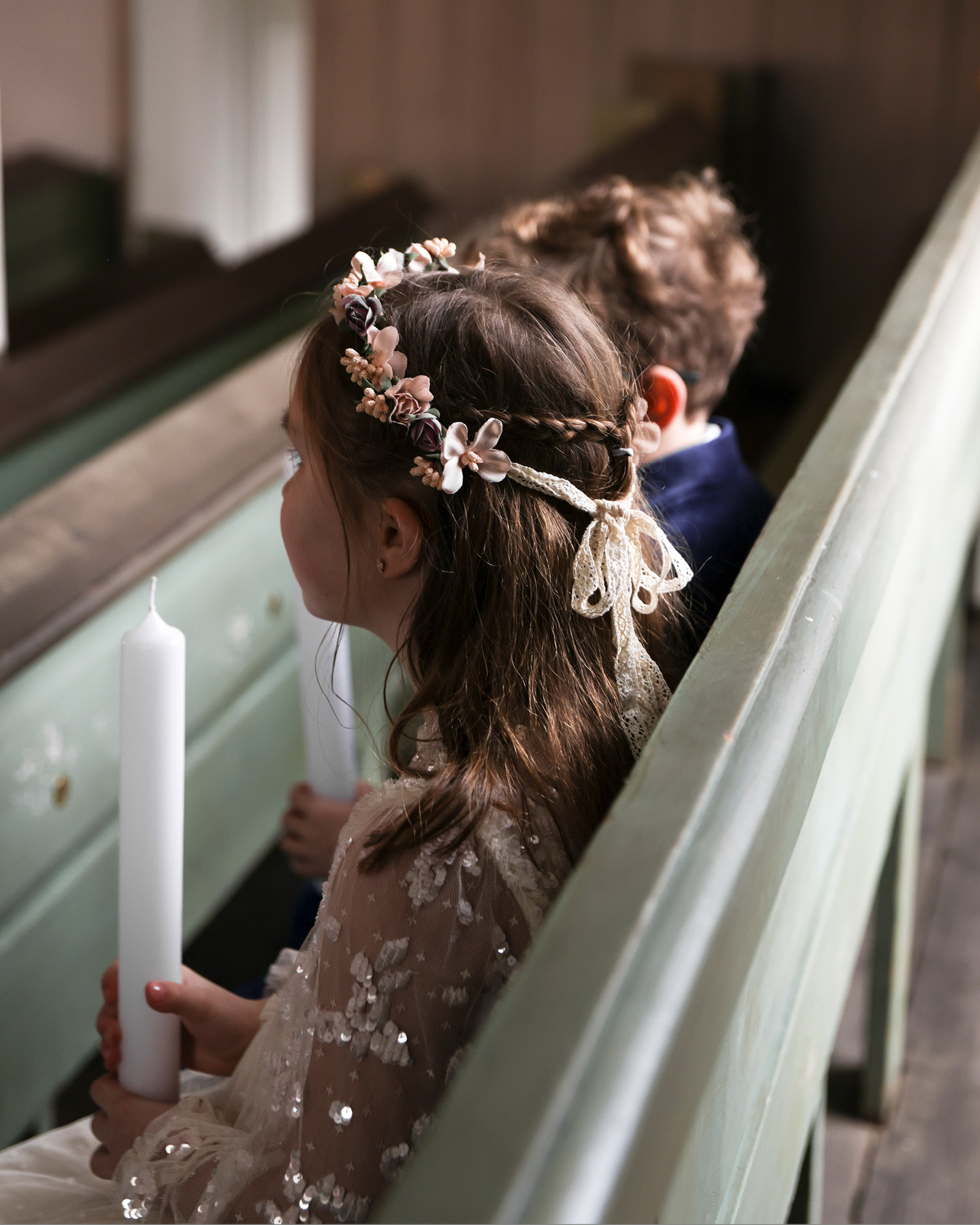 Mädchen und Junge mit Kommunionskerzen in der Hand auf einer Kirchenbank sitzend