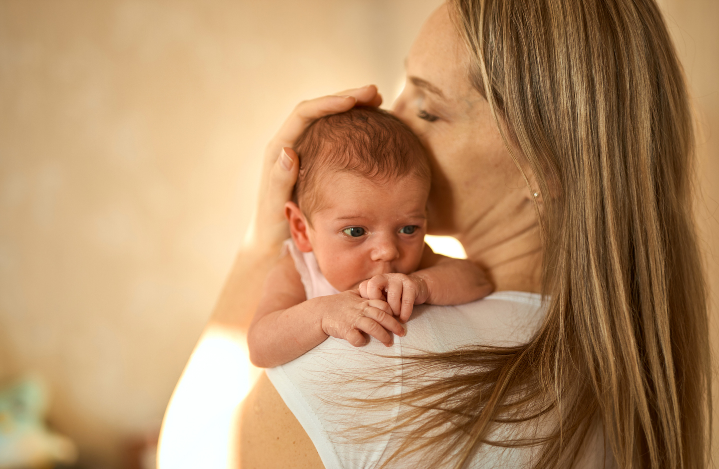 Junge Mutter hat ihr Baby auf dem Arm und küsst es zärtlich