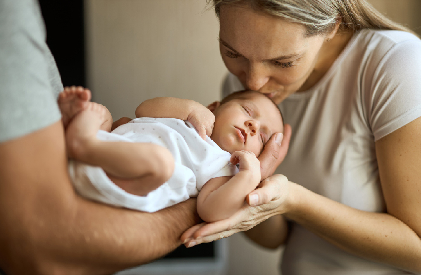 Veter und Mutter halten gemeinsam zärtlich ihr Baby, die Mutter küsst es auf den Kopf