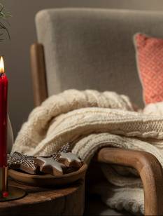 Gemütlicher Sessel mit Decke und Tischchen mit Weihnachtsgebäck und Kerze