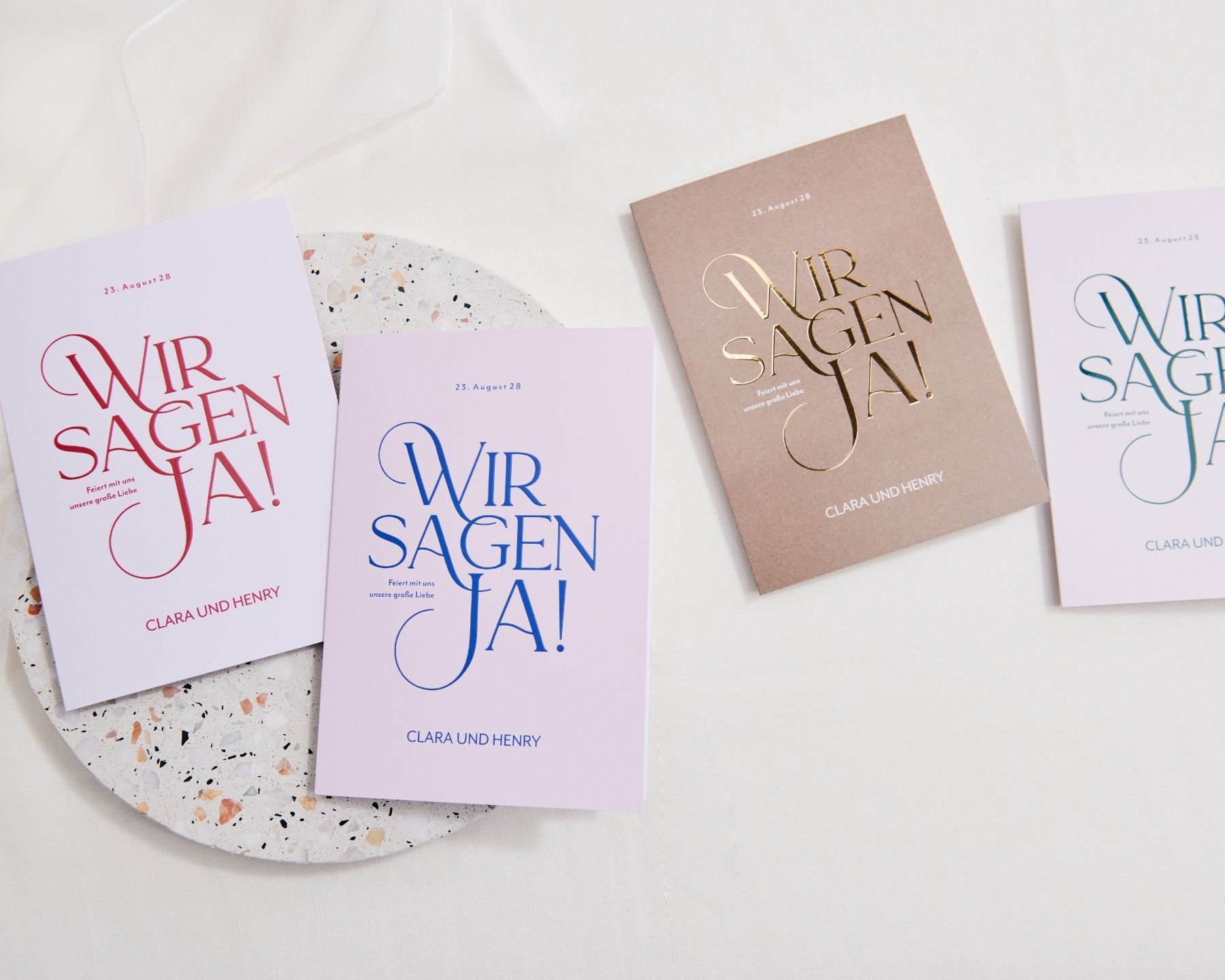 Vier typografisch gestaltete Hochzeitseinladungen in unterschiedlichen Farbenverstreut nebeneinander liegend