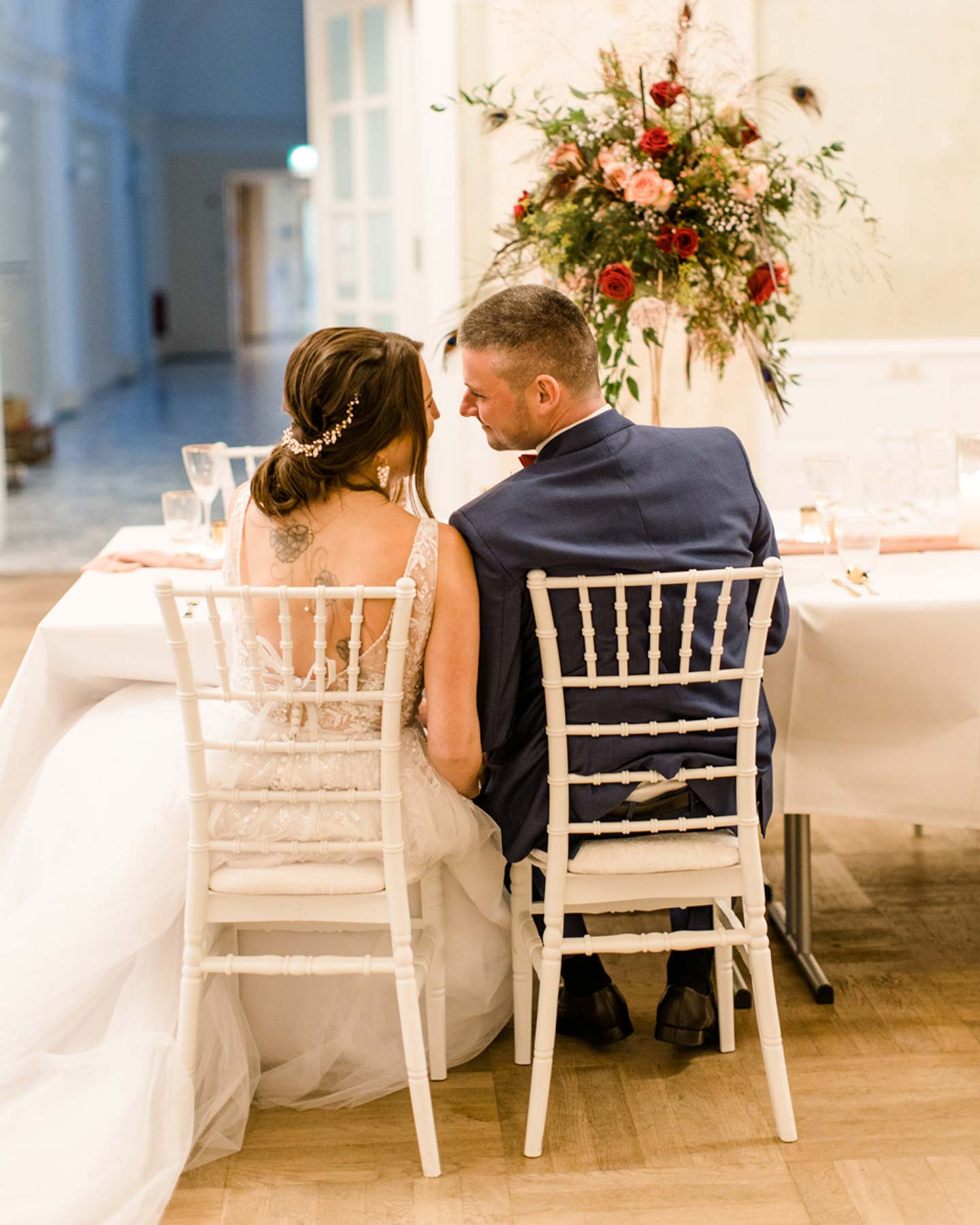 Brautpaar guckt sich an der Hochzeitstafel verliebt an.