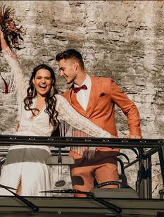 Glückliches Hochzeitspaar posiert lachend in einem Geländewagen vor Felsen