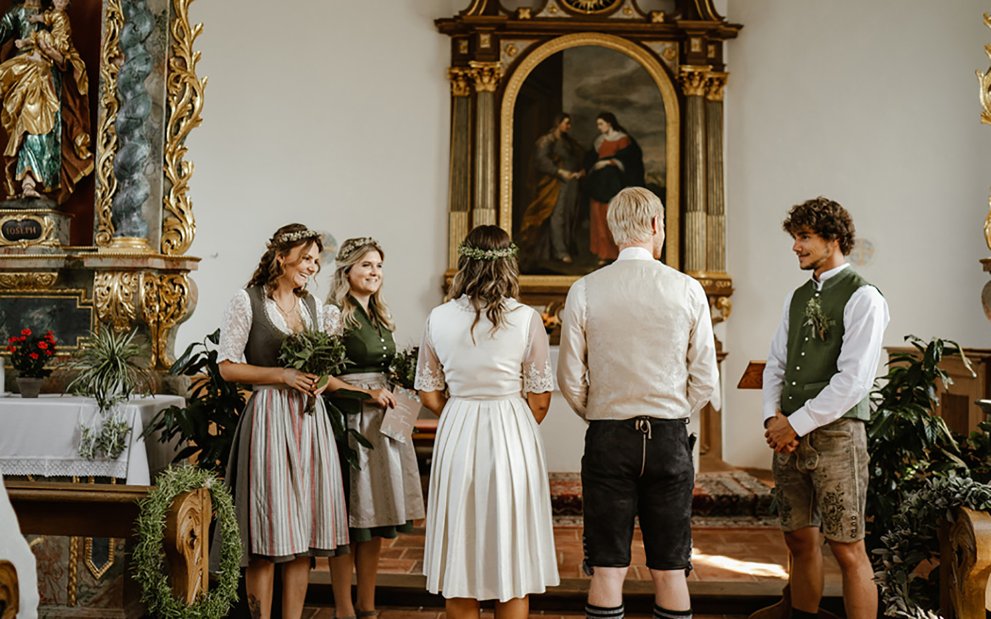 Die Trauzeugen und das Hochzeitspaar stehen vorne in der Kirche. Die Trauung steht kurz bevor, sie sind von hinten vom Eingang der Kirche heraus zu sehen.