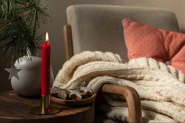 Gemütlicher Sessel mit Decke und Tischchen mit Weihnachtsgebäck und Kerze