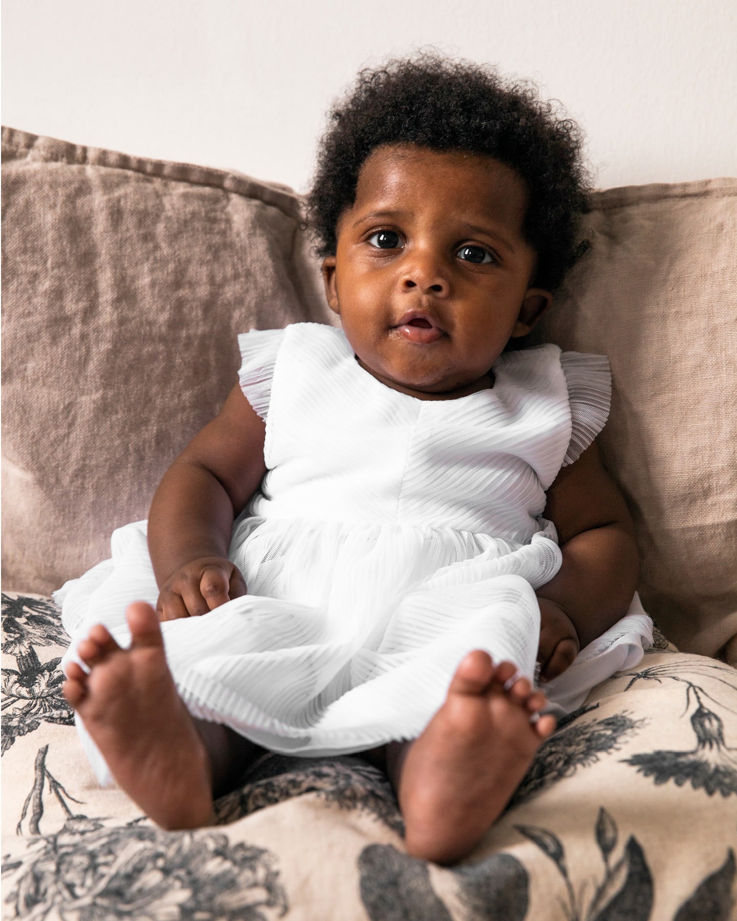 Kleines Mädchen im Taufkleid auf der Couch sitzend