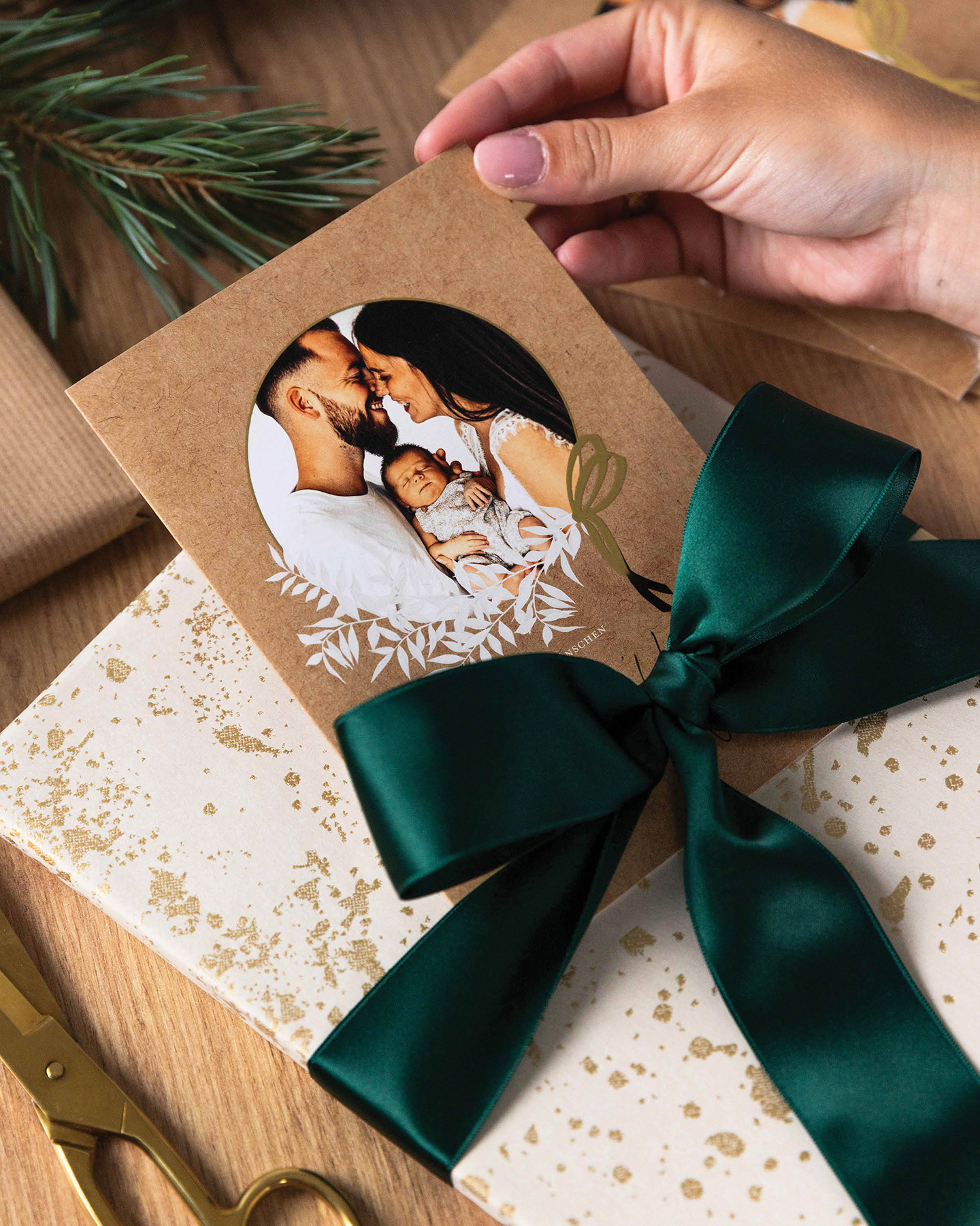 Weihnachtsgeschenk in gold verpackt mit grüner Schleife. Weihnachtskarte wird unter die Schleife geschoben.