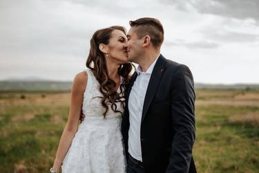 Hochzeitspaar vor ländlicher Kulisse küsst sich liebevoll