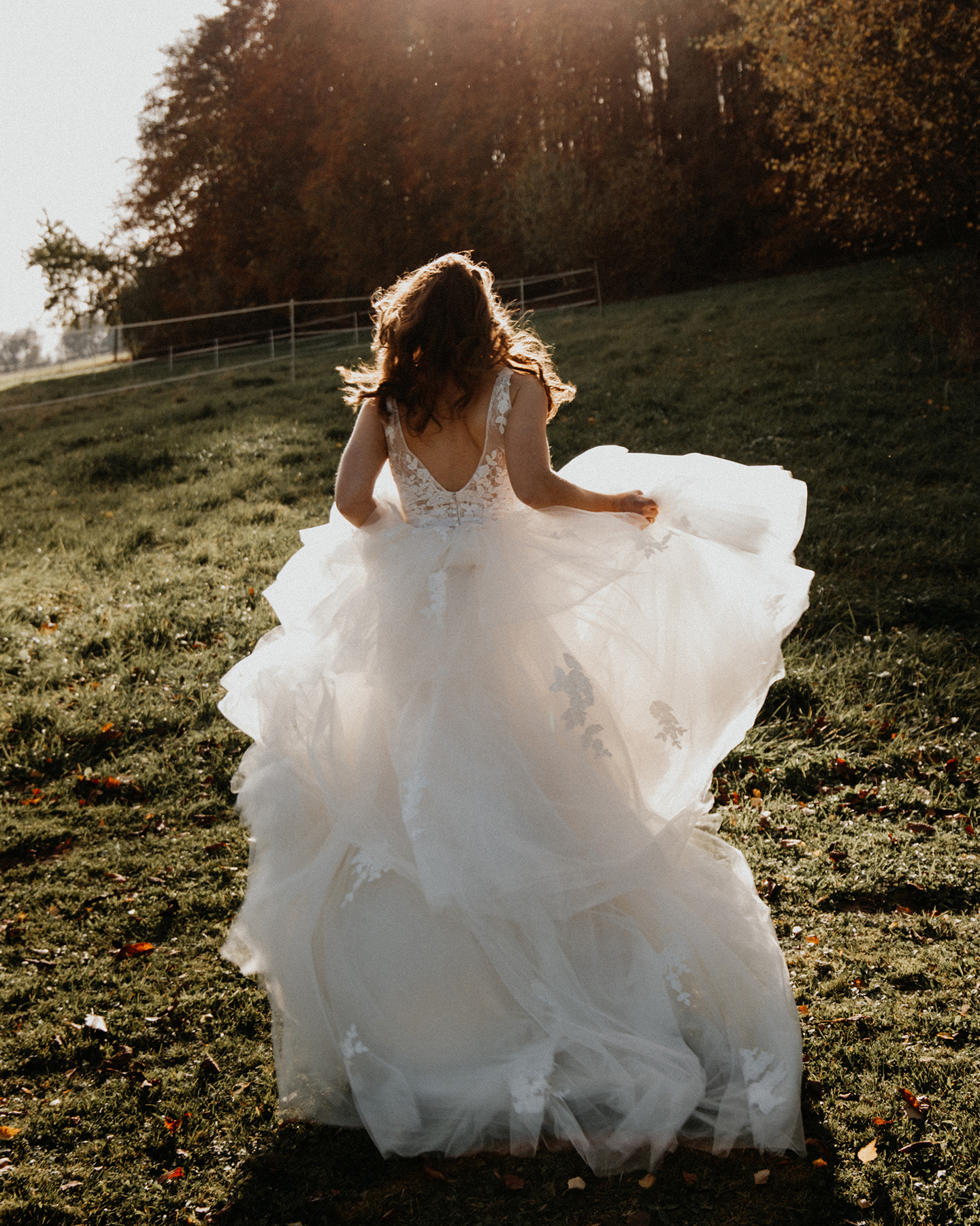 Boho Braut rennt glücklich mit wehendem Brautkleid über eine Wiese bei Sonnenuntergang ihrer Picknick Hochzeit.