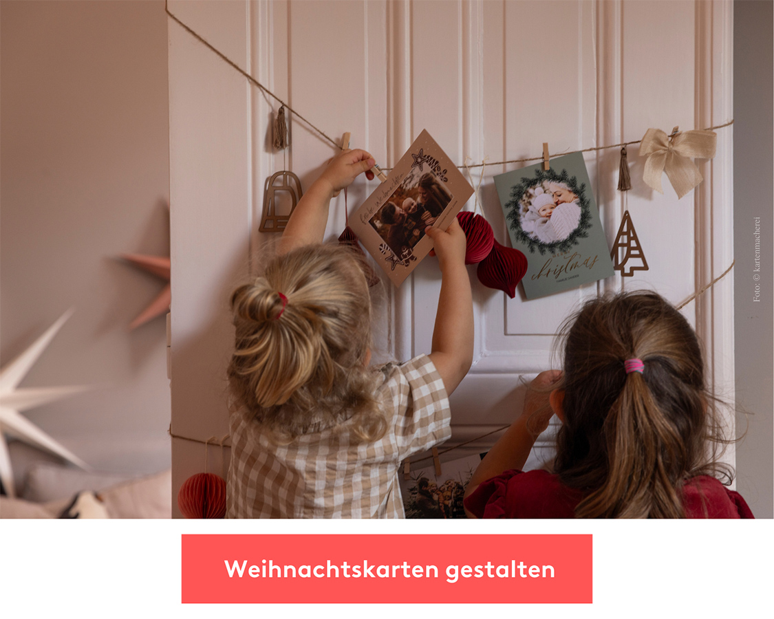 Zwei Kinder befestigen Weihnachtskarten an einer Leine, die an einer Tü hängt.