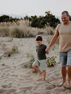 Vater und etwa 8-jähriger Sohn gehen am Vatertag Hand in Hand am Strand spazieren