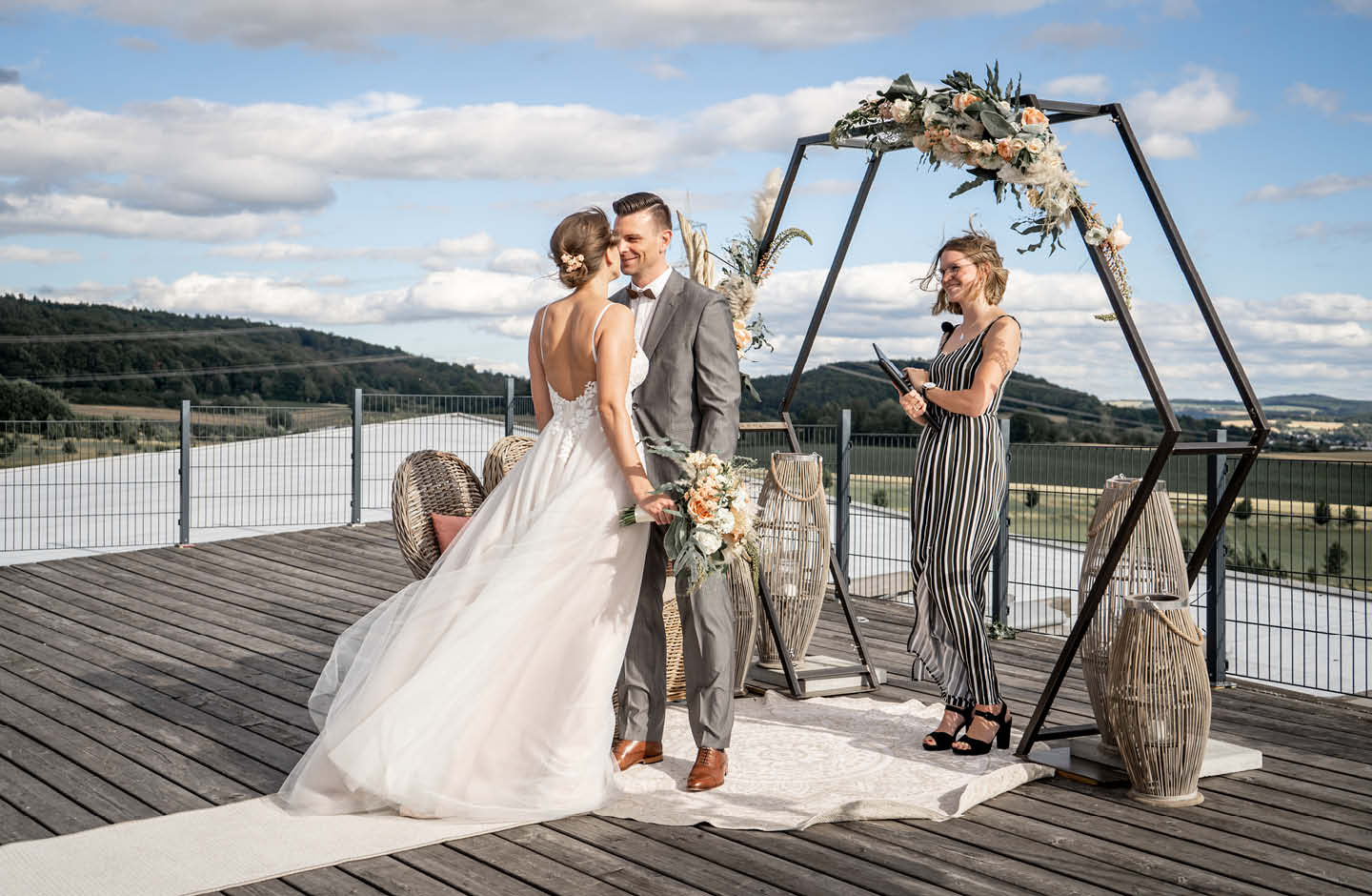 Ein Hochzeitspaar steht draußen vor einem Traubogen.