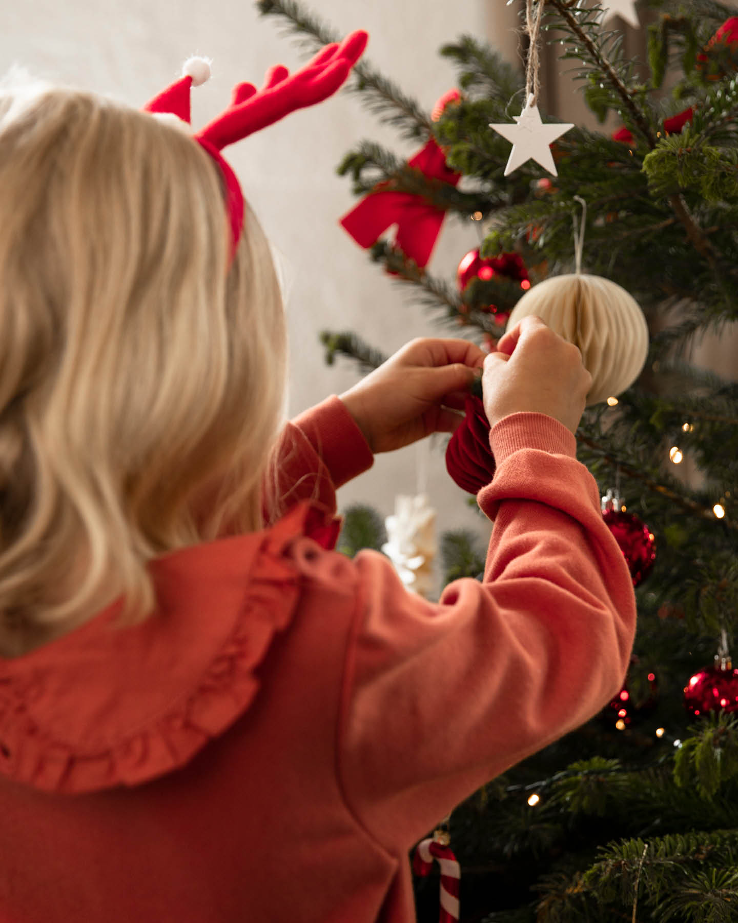 Mädchen in rotem Pullover schmückt einen Weihnachtsbaum.