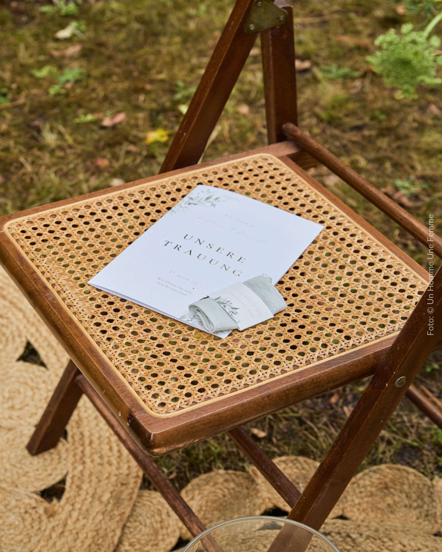 Kirchenheft zur Hochzeit und Freudentränentaschentuch mit personalisierter Banderole liegt auf Stuhl mit Rattangeflecht