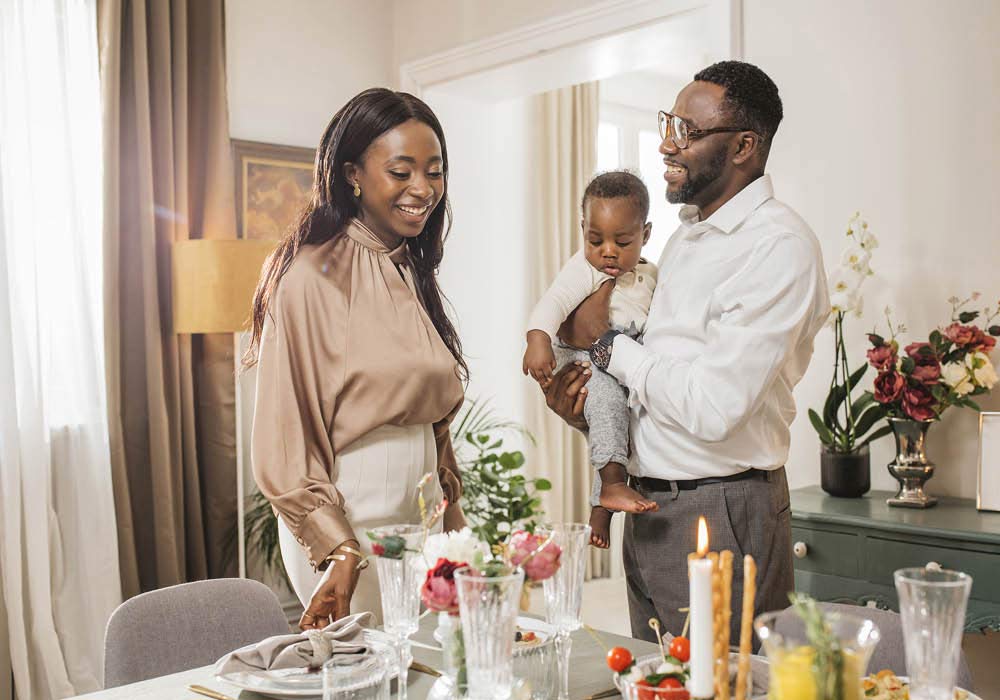 Mama, Papa und Baby stehen glücklich am Esstisch während der Namensgebungsfeier.