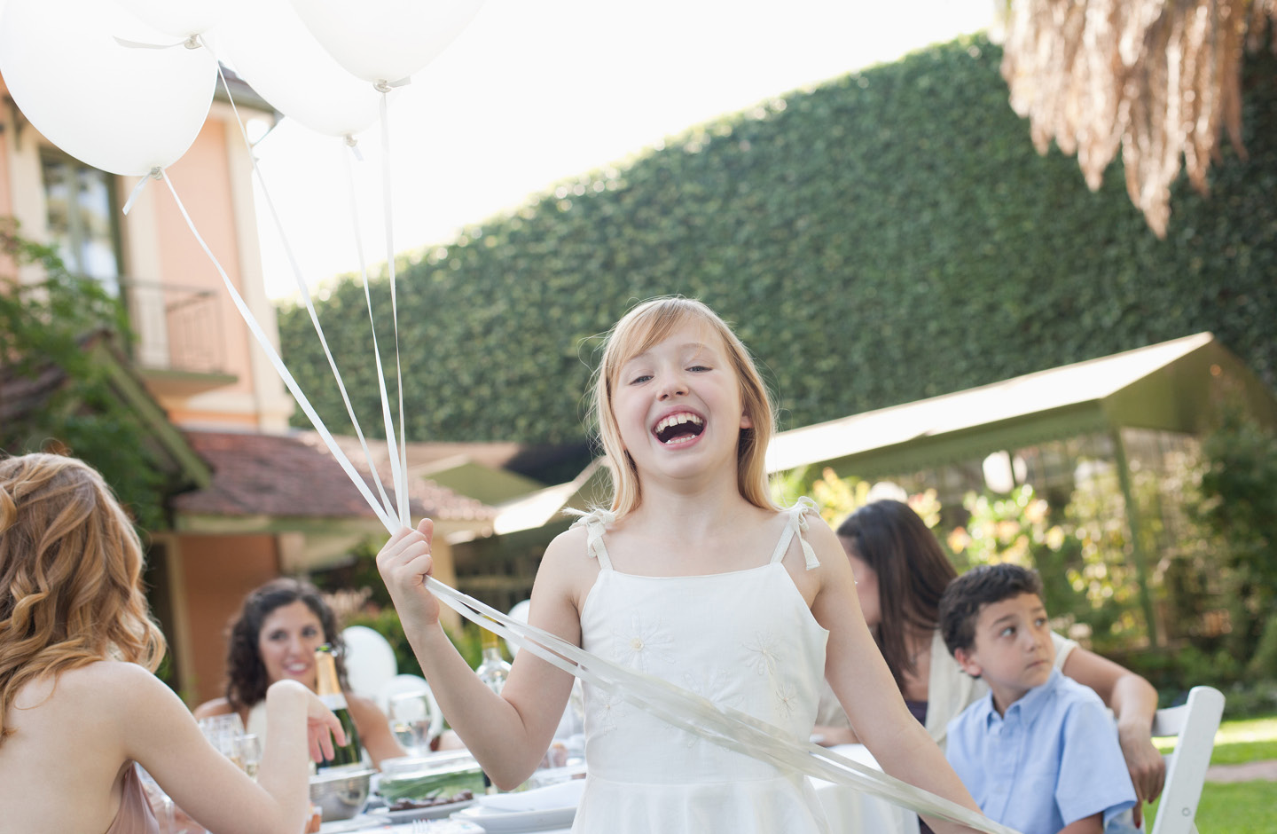 Fröhliches Mädchen mit weißen Luftballons bei einer Taufe im Garten