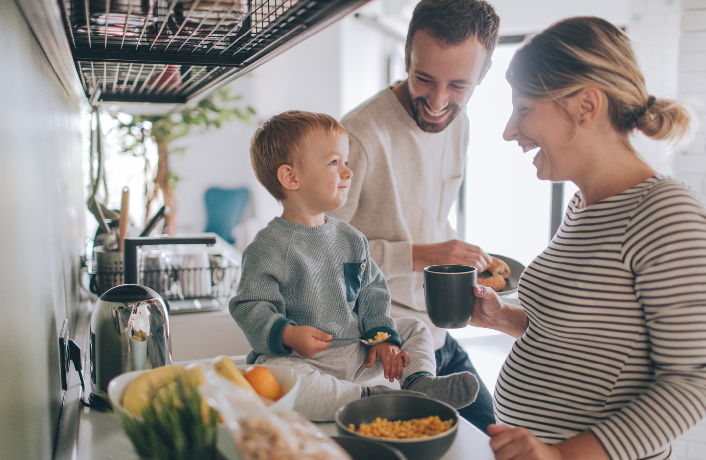 Schwangerschafts Fakten: Schwangere Mama, Papa und Kleinkind essen zusammen Frühstück in der Küche.