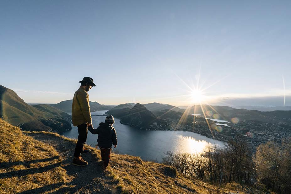 Vater mit Sohn an der Hand blickt auf ein Tal mit großem See
